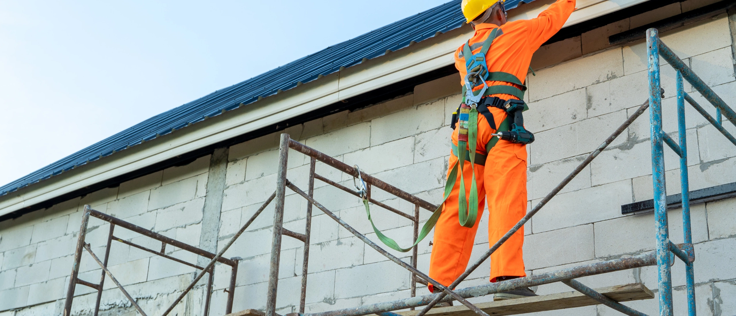 Construction worker wearing a safety harness and helmet while working at height on scaffolding, representing the importance of working-at-heights training in Ontario.