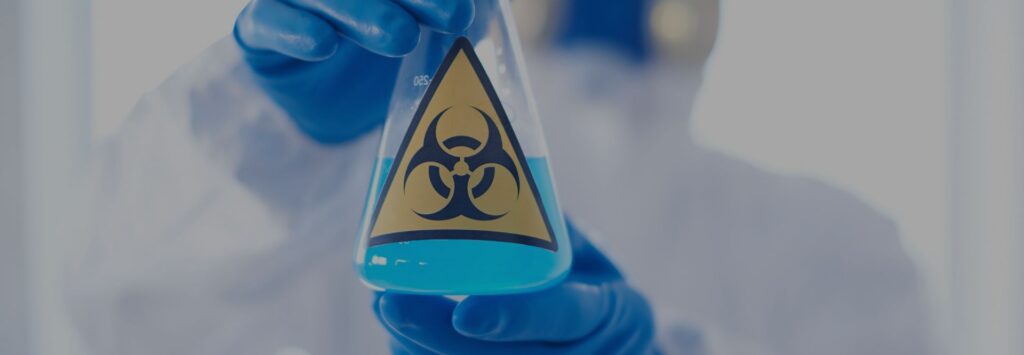 Employee in protective PPE holding a hazardous materials solution during designated substance handling procedures.