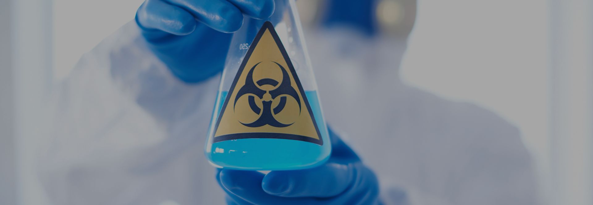 Employee in protective PPE holding a hazardous materials solution during designated substance handling procedures.